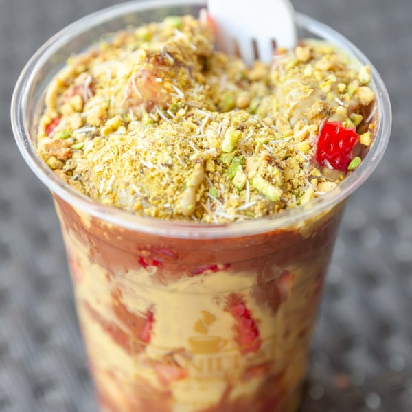 A Vanilla Espresso French Café dessert cup filled with layers of cream, chocolate, and fruit, topped with pistachios.