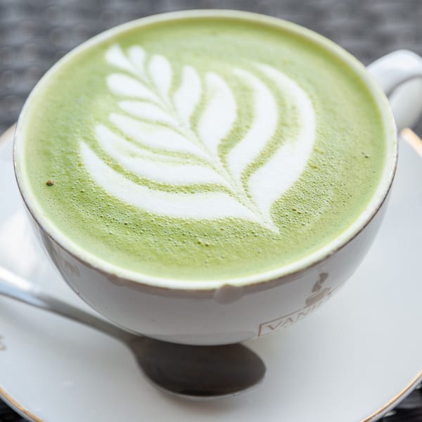A vibrant green matcha latte with delicate white latte art in a Vanilla Espresso cup.