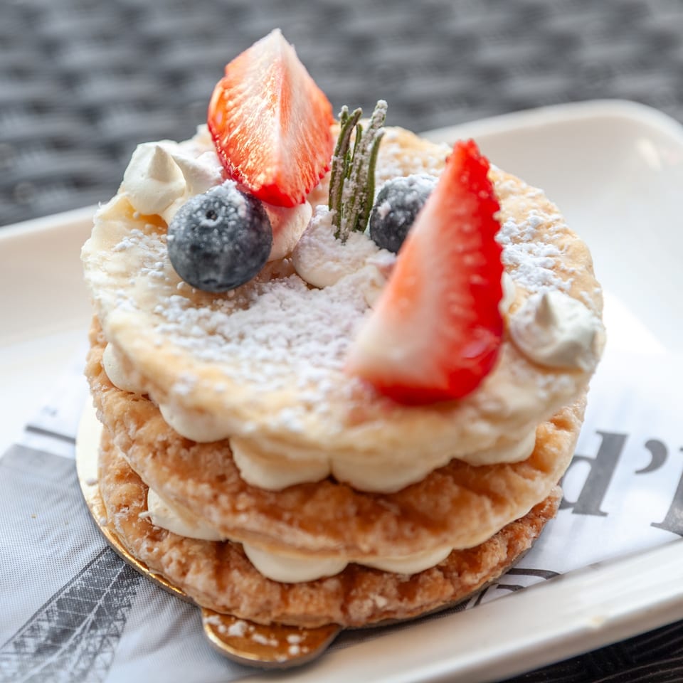 Vanilla Espresso French Café's mille-feuille with strawberries, blueberries, and powdered sugar on a white plate.