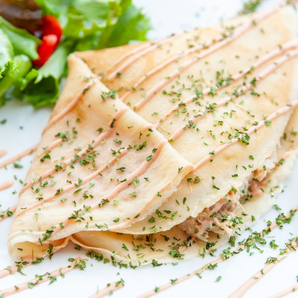 Savory French crepe drizzled with sauce and herbs, served with a side salad.
