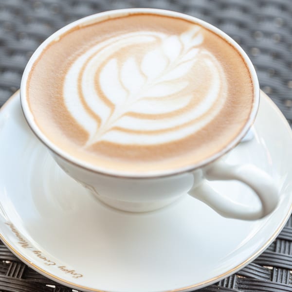 Close-up of a latte with intricate leaf-shaped latte art in a white cup and saucer.